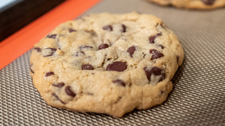 A close-up of a choc-chip cookie on a silicone baking mat.