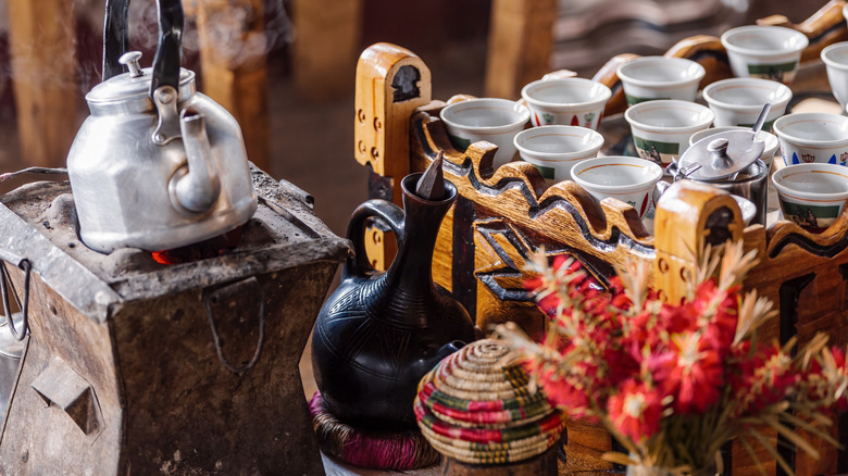 A bunna ceremony set up with many small cups next to a jebena and hot water kettle