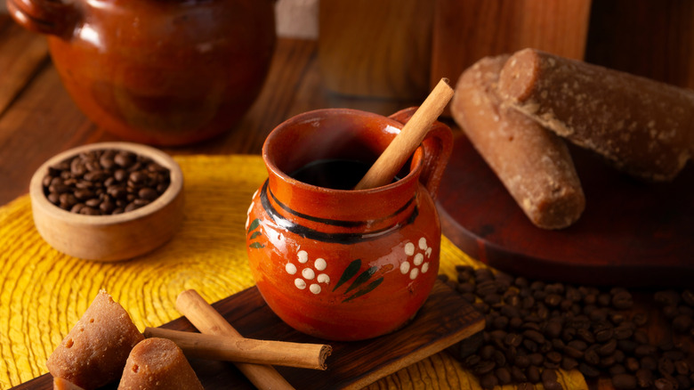A clay pot of cafe de olla with a cinnamon stick and piloncillo in the background