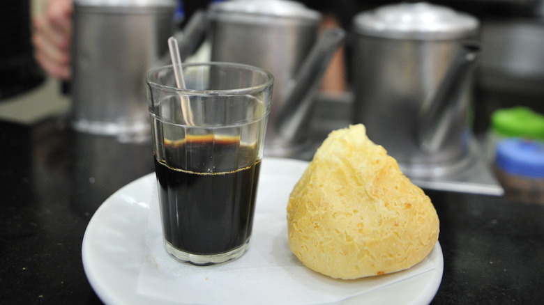 A small glass of black cafezinho on a plate with a Brazilian cheese puff