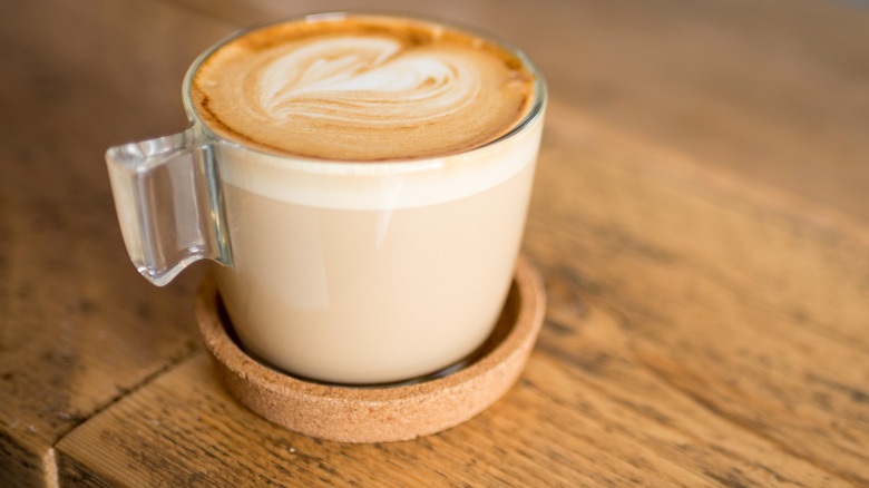 A flat white in a glass mug on a wooden table