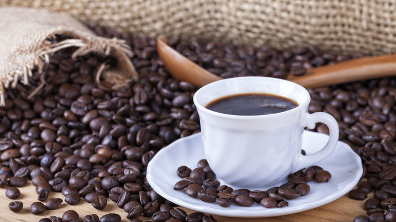 A white mug with black coffee on a pile of coffee beans