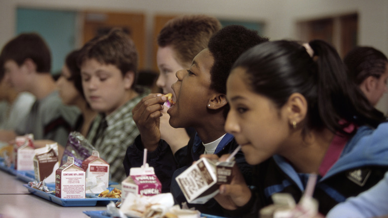 Kids sitting at a lunch table with trays of food and cartons of milk