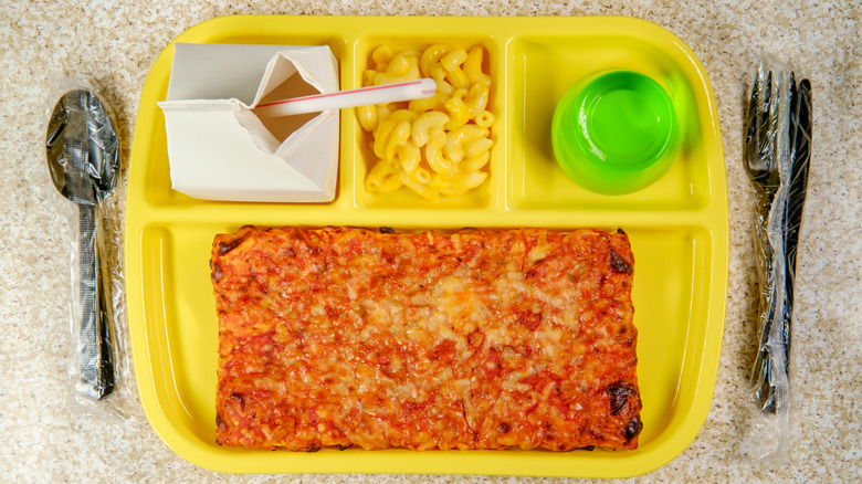 A plastic lunch tray with pizza, macaroni and cheese, and green jello