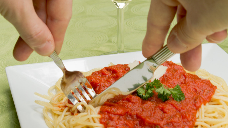 A person cutting spaghetti with a knife and fork