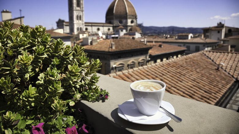 A cappuccino sitting on a ledge overlooking an Italian city
