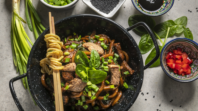 Chopsticks with noodles resting on a bowl of beef udon