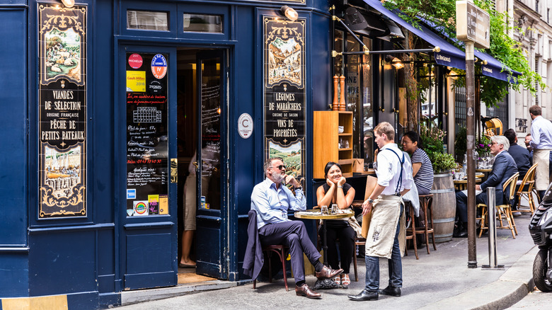 A server talking to customers outside a Parisian cafe
