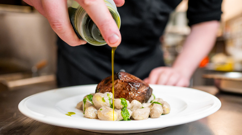 A chef drizzles some olive oil over a dish