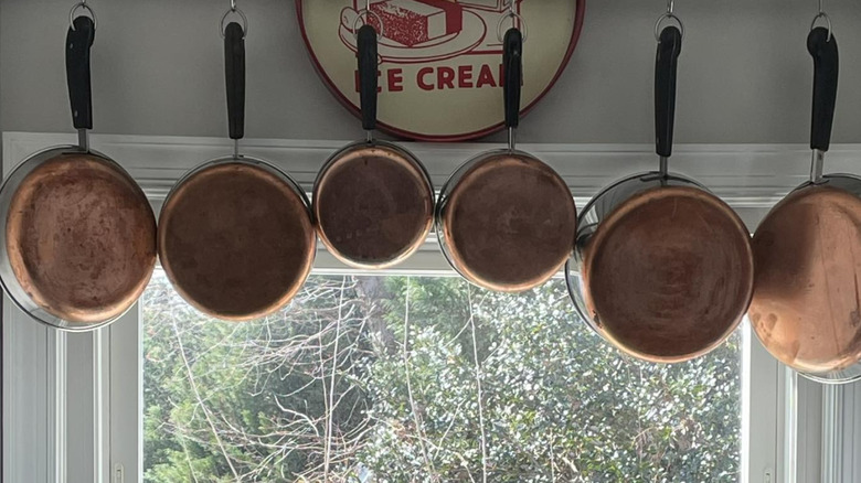 Various Revere ware pots and pans hanging on display