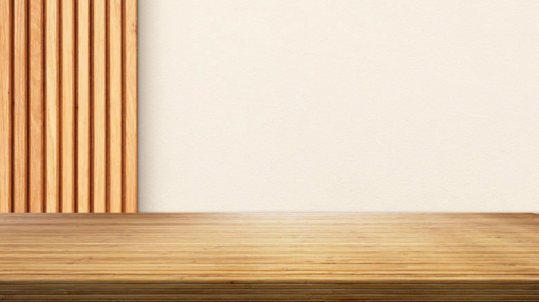 A smooth bamboo countertop in front of a white wall with wood panels on the side.