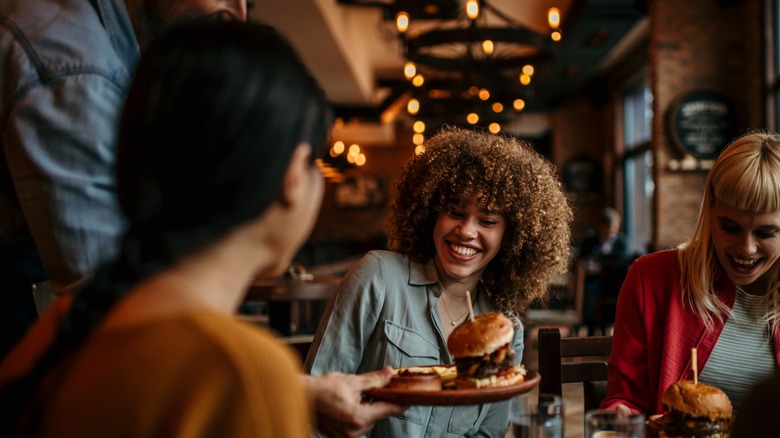 Waiter delivering steak burgers to happy customers.