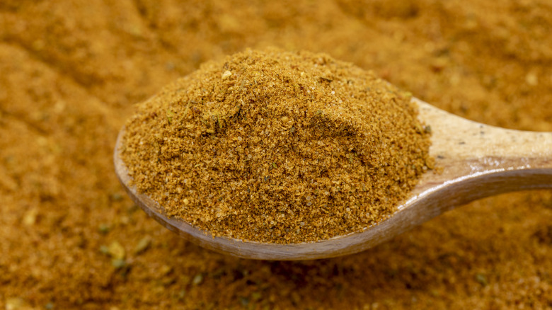 A wooden spoon scoops dusty red Cajun spice from a larger pile of the seasoning