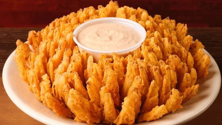 A golden, crispy fried onion blossom with a ramekin of light pink creamy sauce in the center