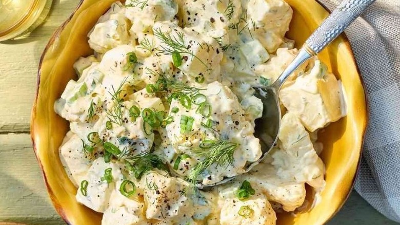 Bowl of potato salad topped with herbs and green onions