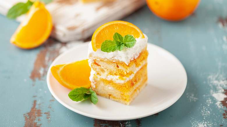 Slice of orange cake top with fluffy frosting, mint, and an orange slice
