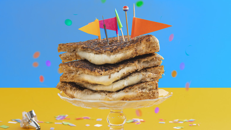 A festive grilled cheese topped with colorful flags and surrounded by confetti