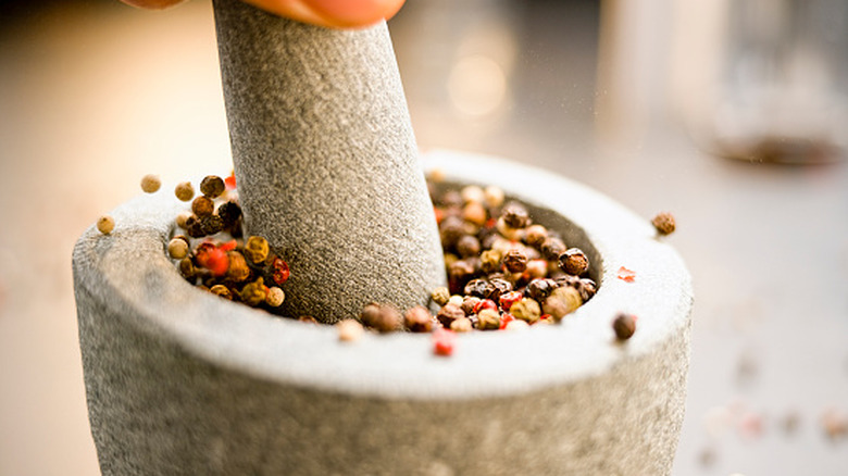 An individual crushing pepper into a mortar and pestle.