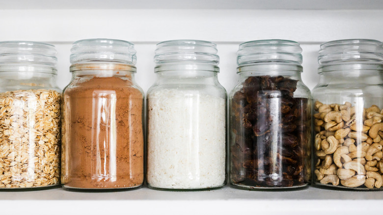 Glass jars containing assorted dry foods lined up on a white shelf