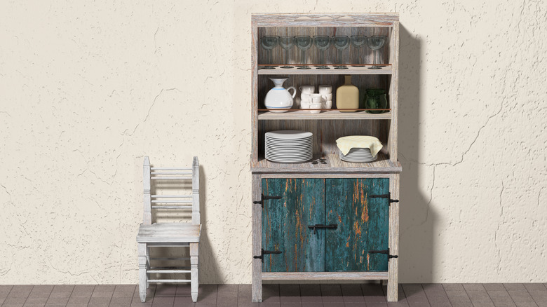 A gray and teal kitchen hutch filled with dishes sits against a textured wall