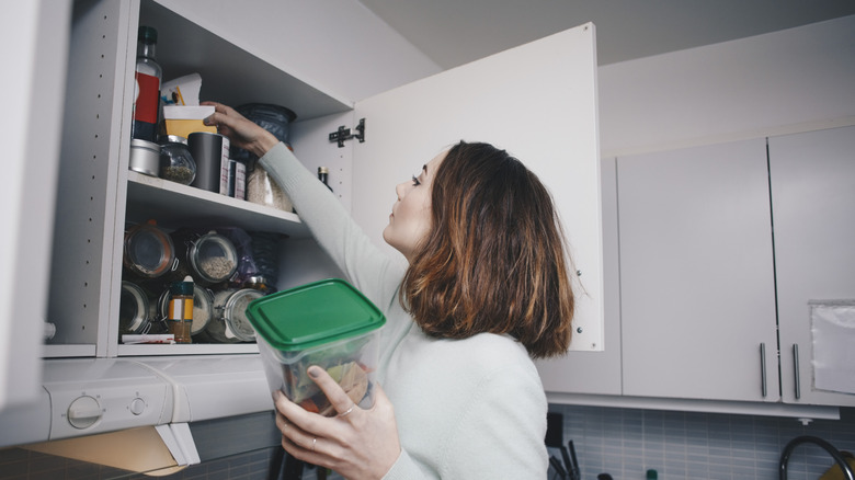 A woman takes items out of a kitchen cabinet