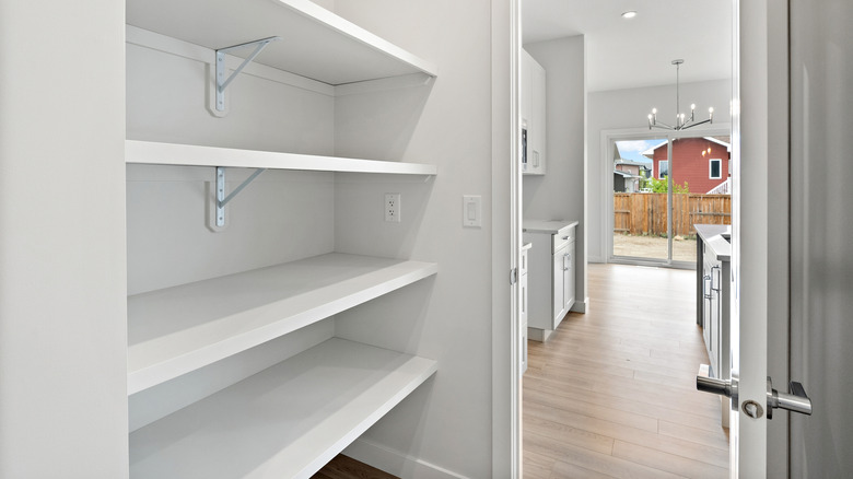 Empty white pantry shelves with a kitchen in the background