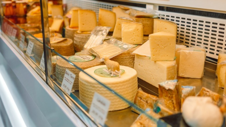 Artisanal cheeses for sale in an open cooler at a grocery store.