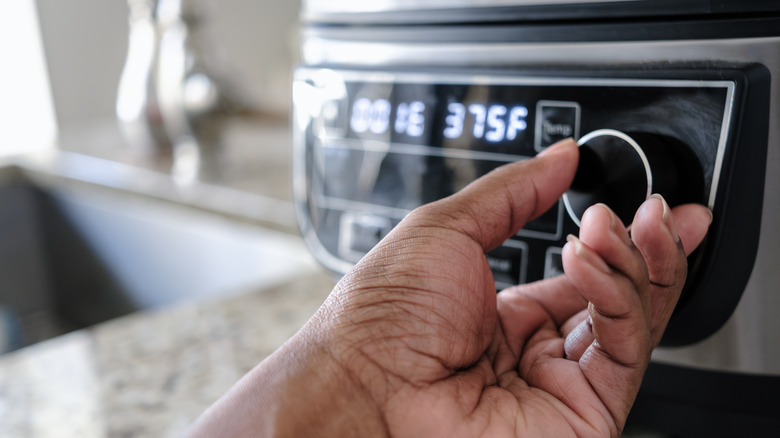 A hand adjusting a dial on an air fryer