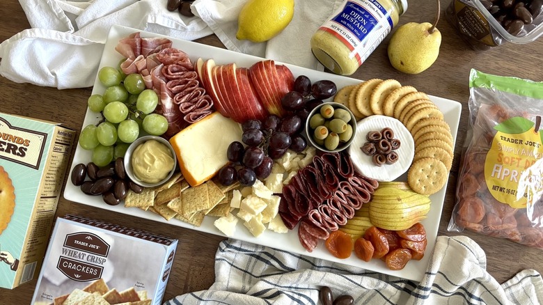 charcuterie board on walnut table surrounded by foods