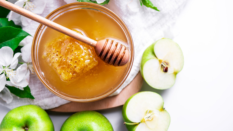 Apples and honey in a glass ramekin with white flower blossoms