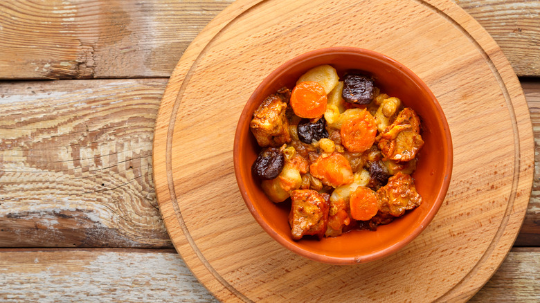 Decorative orange bowl of tsimmes on a round wooden cutting board