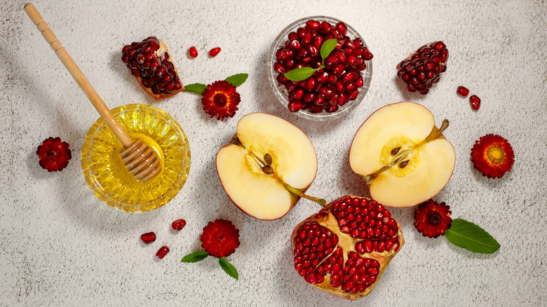 Apple halves, pomegranates, and a glass ramekin of honey