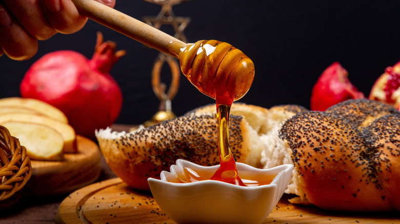 Honey in a ramekin, challah, pomegranates, and other Rosh Hashanah symbols on wooden cutting boards