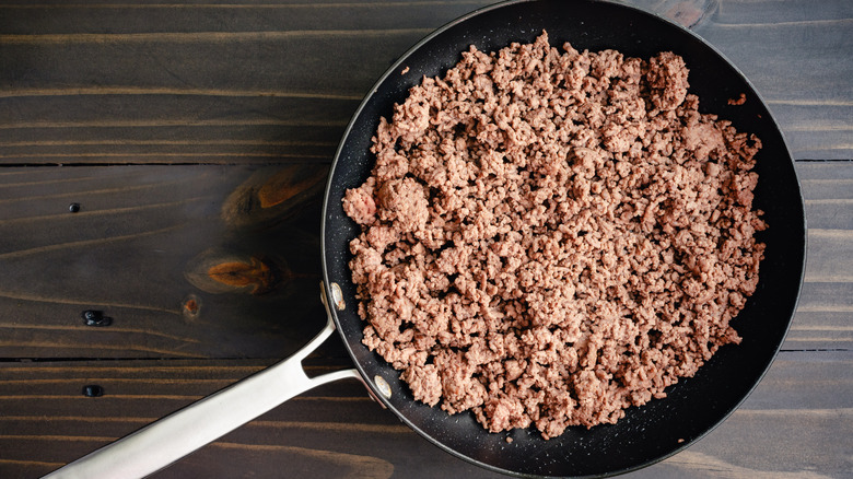 Cooked ground beef in a pan set on a wood background