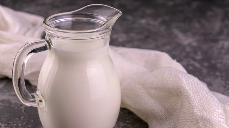 A jug of milk on a grey background, muslin behind it.