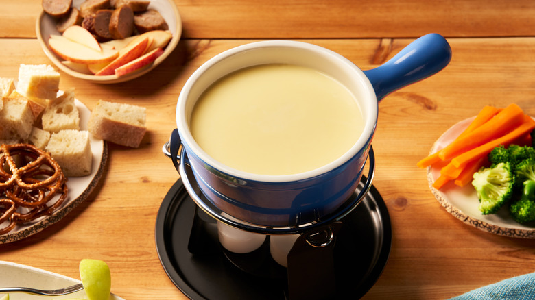 Pot of cheese fondue surrounded by pretzels, bread, vegetables, and other dippers