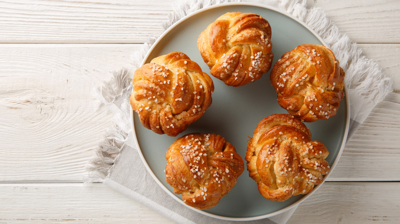 Five yeast knot sugar buns on a plate sitting on cloth napkin on wood surface.