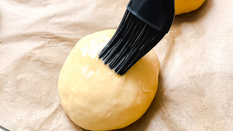 An individual brushing egg wash on a ball of dough.