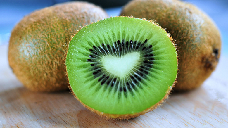 A halved kiwi on a wooden board with whole ones