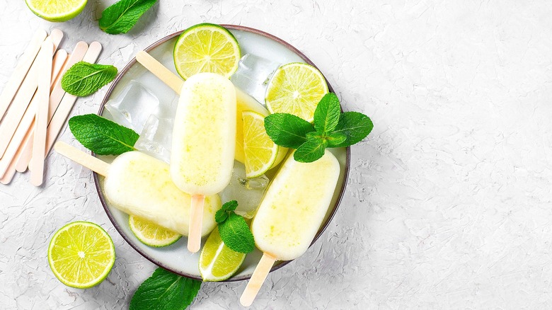 Plate of lime popsicles surrounded by limes and mint leaves