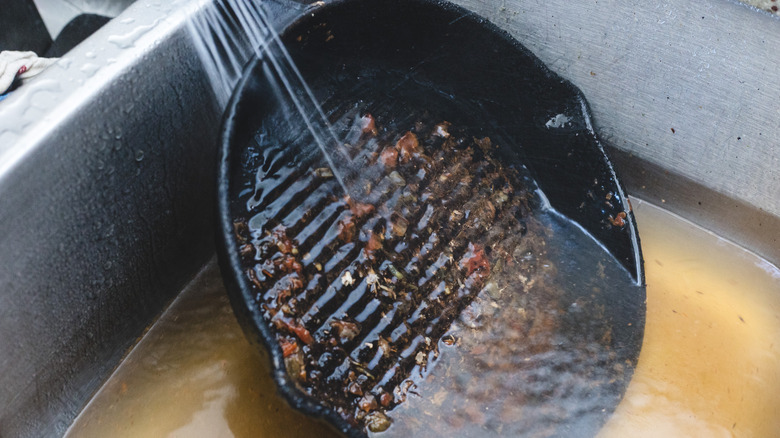 Rinsing a dirty cast iron pan under hot water