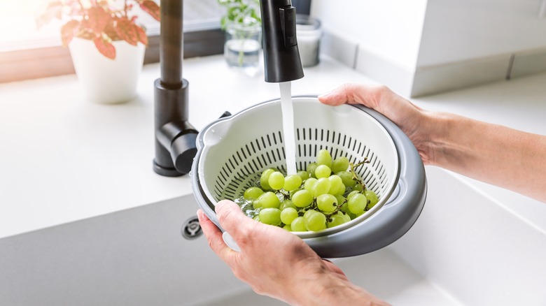 Hands washing grapes in a colander over the sink