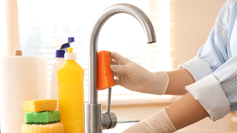 woman cleaning a kitchen faucet with a sponge