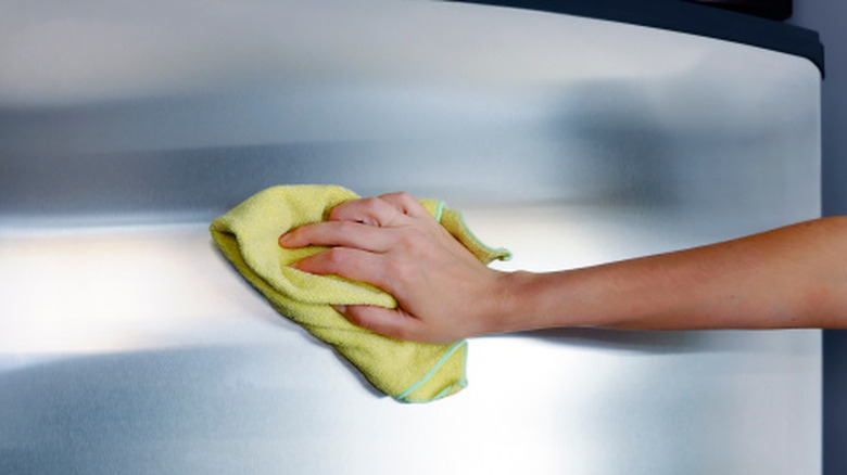 hand wiping stainless steel fridge with a microfibre cloth