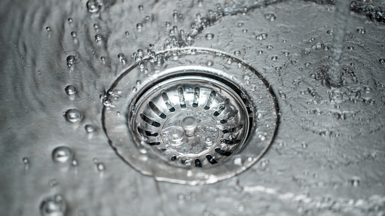 Stainless steel kitchen sink with water pouring down the drain.