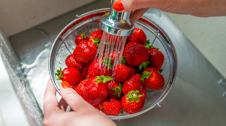 Hands rinsing strawberries with water