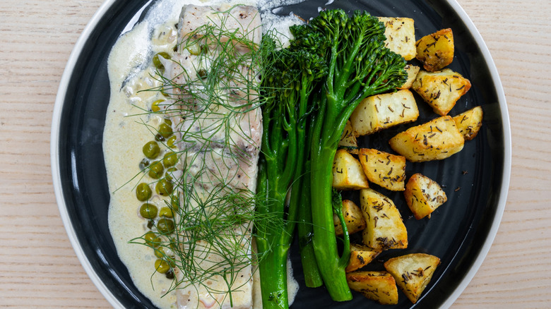 A plate of cooked fish with broccolini and potatoes.