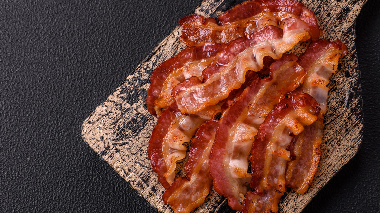Slices of cooked bacon on a wooden board with a black background