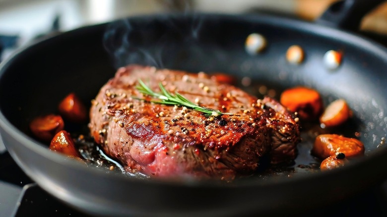 Steamy pan-seared steak in a coated frying pan topped with fresh rosemary