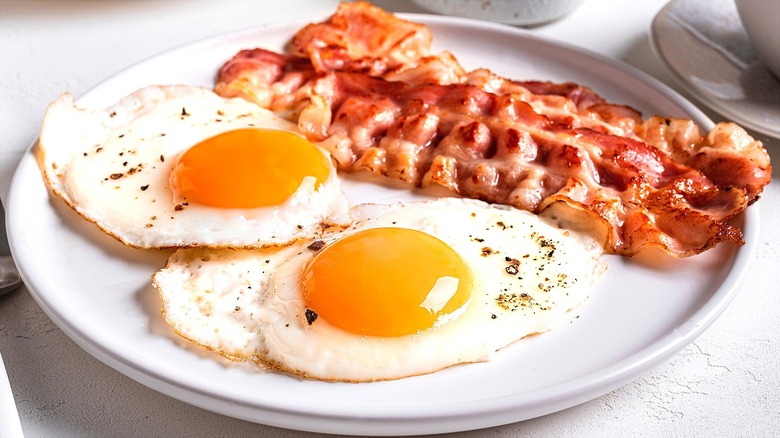 Two fried eggs with cracked pepper and bacon on a white plate